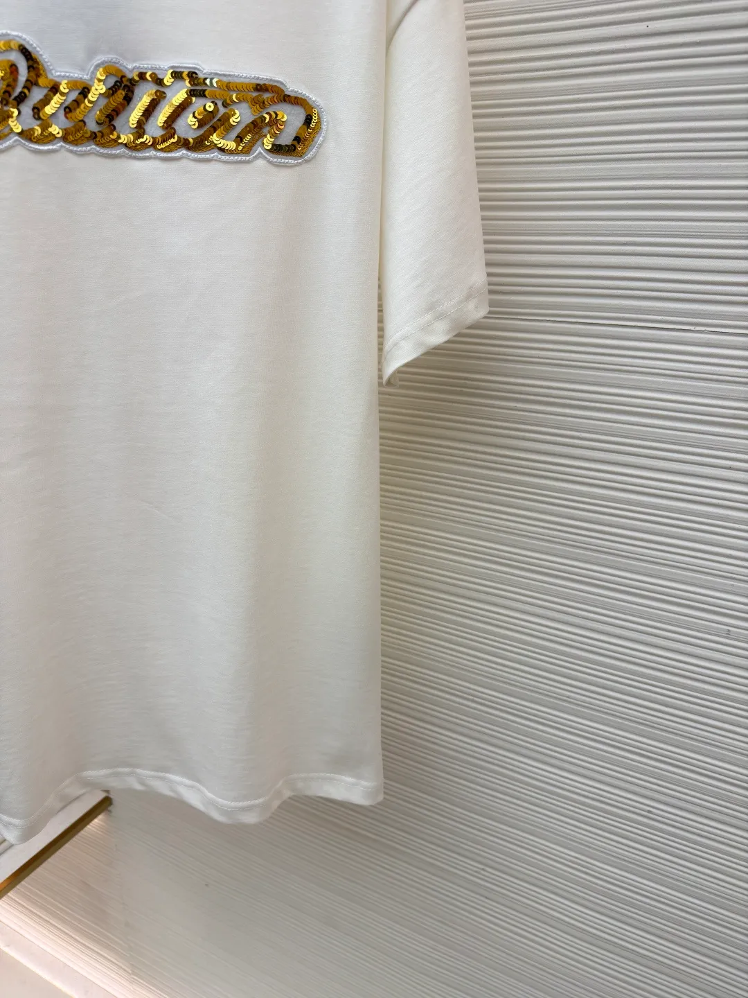 LOUIS VUITTON cotton round neck embroidered Vuitton signature logo short sleeves ●Original version: purchased and developed for 12300 ●Item number: 1682272-A10 ●Fabric: cotton fabric ●Technology: embroidery production ●Color: white ●Version: fitted version ●Weight: about 270 grams ●Size: S-M-L-XL ●Description: This white short-sleeved T-shirt is made of high-count combed cotton fabric and has been treated with pre-washing technology. It has a soft and skin-friendly touch and is not easy to deform. The silhouette of the shirt is a loose shoulder design, which meets the needs of modern casual wear. The core decoration area on the chest uses hand-beading and bronzing technology, and uses metallic gold sequins and embroidery threads intertwined to outline a three-dimensional letter pattern. The sequins are layered and inlaid, and each one is manually positioned and fixed by craftsmen to ensure a regular texture and uniform gloss. The edges of the letters are sewn with matte silk thread to form a visual contrast between gold and matte, while reinforcing the decorative structure to avoid falling off during wear. The neckline uses double-needle hemming technology and is matched with ribbed cuffs of the same fabric. It is durable and fits the neck. The overall craftsmanship combines handicraftsmanship with modern clothing technology, and the details show exquisite texture. The overall wiring is straight and delicate, the fabric is comfortable and soft, and the color is consistent without color difference. It can be matched with the same style to create a fashionable look and control various occasions. Customized accessories, complete with three standards, same style for men and women!